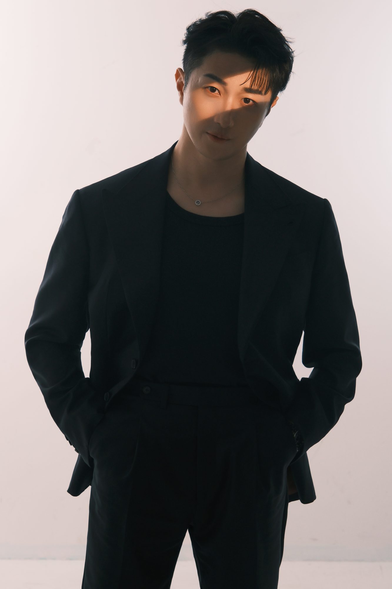 Editorial studio portrait of John Fung in a black suit against a warm ivory backdrop
